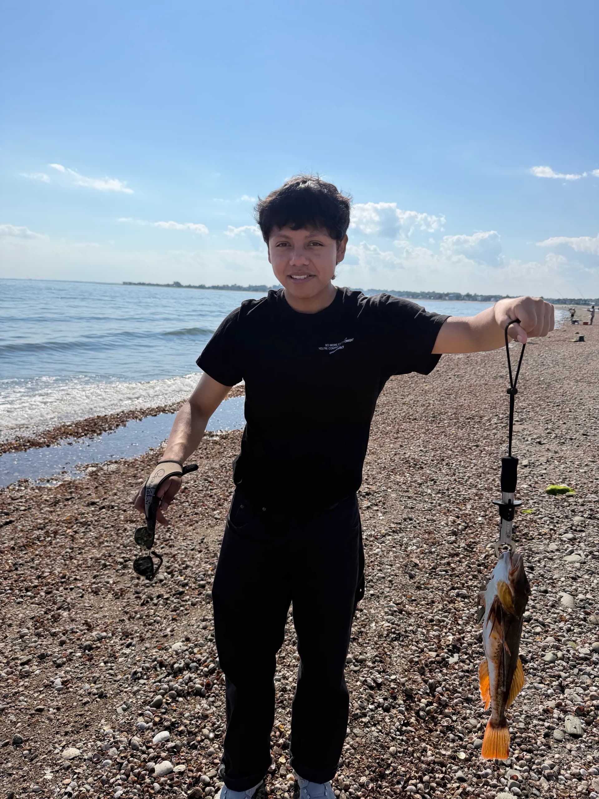 Herb on a shell beach holding the sea robin at arm's length by the line, sunglasses in his other hand